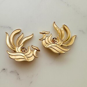 May include: A pair of gold-tone metal earrings shaped like stylised phoenixes with detailed feather designs.