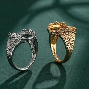 Pode incluir: Dois anéis de prata e ouro com um design floral. Os anéis são abertos na frente e têm um espaço para uma pedra ou outro adorno.