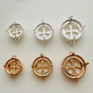 May include: Four silver and gold cross-shaped pendant settings with a round bezel. The settings are in two sizes, with the larger settings having a rope-like edge.