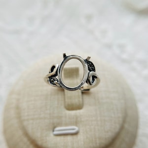 Può includere: Anello in argento con una montatura ovale e accenti di marcasite nera. L'anello è progettato con un motivo delicato e a spirale.