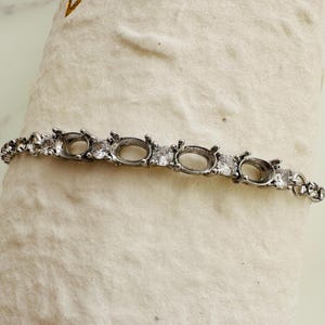 Peut inclure: Un bracelet en argent avec des montures ovales pour des pierres. Le bracelet est orné de petites pierres de zircone cubique transparentes.