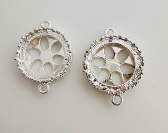 May include: Two silver-toned, round jewelry components. Each component features a floral design in the center and a textured border. They have small loops for connecting to other pieces, perfect for jewelry making.