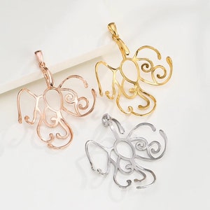 May include: Three ornate metal pendant bails in gold, rose gold, and silver. Each bail features a delicate, intricate design with swirls and curves.