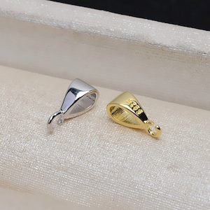 May include: Two silver and gold pendant bails with a loop on one end and a flat surface on the other. The gold bail has the inscription "925" on the flat surface.