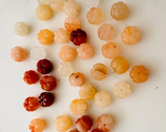 May include: A collection of small, carved, flower-shaped beads in shades of white, peach, orange, and red. The beads are made of agate and are perfect for jewelry making.