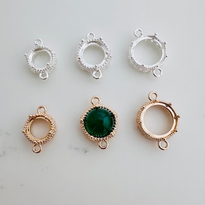 May include: Six silver and gold-toned metal settings for jewellery making. The settings have a round bezel and two loops for attaching to a chain or cord. One setting has a green glass cabochon.