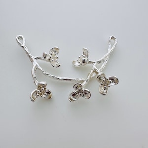 May include: Silver pendant featuring a delicate branch with five small flower blossoms. The branch is textured and the flowers have a detailed design.