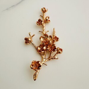 May include: A gold-toned metal branch with delicate, detailed flowers. The branch is stylized to resemble a flowering tree branch.