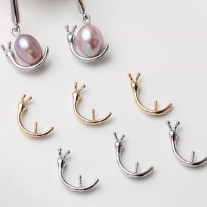May include: A set of six snail-shaped earring findings, two with pink pearls, two gold-toned, and two silver-toned.