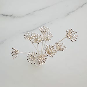 以下が含まれることがあります： 小さな丸いボールのクラスターが付いた、銀の花の形をしたピックのセット。ピックは花瓶のような形に配置されています。