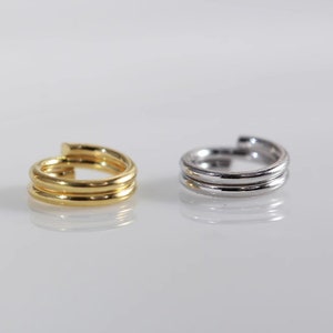 May include: Two simple, minimalist ear cuffs. One is gold and the other is silver. Both are made of a thin, smooth metal and have a simple, rounded shape.