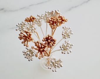 May include: A bouquet of small, delicate flowers made of silver and copper wire. The flowers are arranged in a clear glass vase.