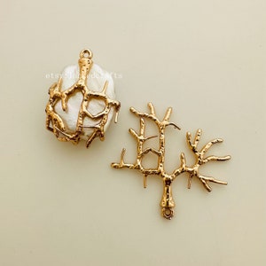 May include: Two gold-toned metal jewelry findings in the shape of a branch. One finding is a pendant with a large, white pearl in the center. The other finding is a branch with a loop at the bottom.