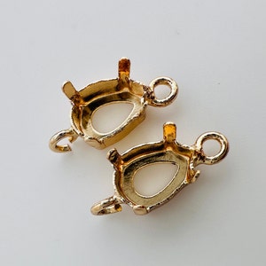 May include: Two gold-tone metal pendant settings with a teardrop-shaped opening for a stone or gem. Each setting has a loop for attaching to a chain or cord.