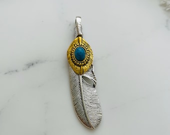 May include: A silver feather pendant with a gold-toned center featuring a turquoise stone. The pendant is a popular design for jewelry making.