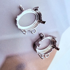 Peut inclure: Deux montures de bijoux en métal argenté présentant des cadres de forme ovale avec plusieurs griffes pour le sertissage de pierres. Chaque monture comprend une petite boucle circulaire en haut et en bas pour relier des chaînes ou des éléments.
