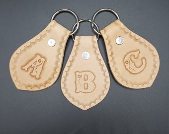May include: Three leather keychains with the letters A, B, and C embossed on them. Each keychain has a scalloped edge and a silver metal ring. The keychains are tan and have a silver snap closure.