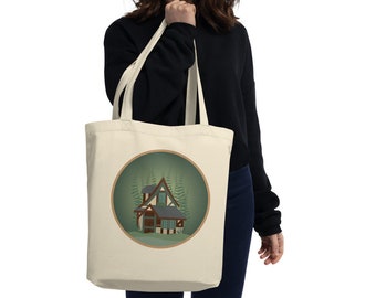 Puede incluir: Una bolsa de tela beige con un diseño circular que representa una escena de bosque verde con una casa marrón y blanca.
