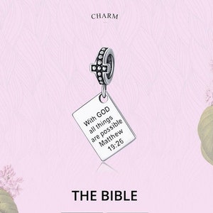 May include: Silver charm with a cross and a rectangular tag that reads "With God all things are possible Matthew 19:26". The charm is on a pink background with flowers.