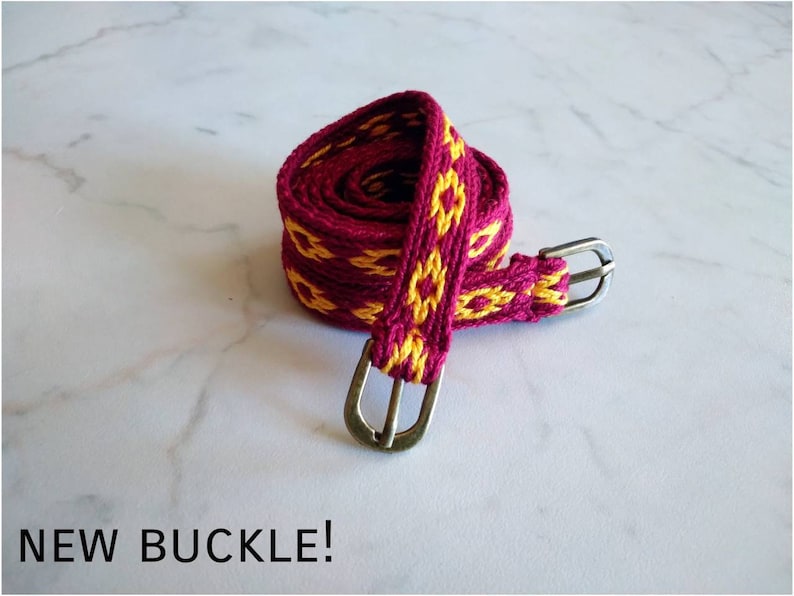 May include: A woven belt with a burgundy and yellow pattern and silver buckles. "NEW BUCKLE!" is written in black text below the belt.