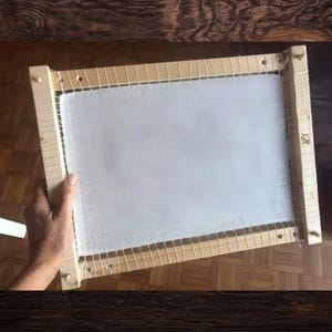 Może przedstawiać: Drewniany tamborek do haftu z białą tkaniną rozciągniętą na nim. Tamborek jest wykonany z naturalnego drewna i ma prosty design. Tkanina jest gładka i napięta, gotowa do haftowania.