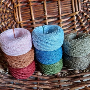 May include: Six spools of yarn in a wicker basket. The yarn is in various colours, including pink, blue, brown, green, and grey.