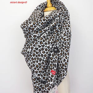 Könnte beinhalten: Ein Leopardenmuster-Loop-Schal in Schwarz, Braun und Weiß. Der Schal ist über einem hölzernen Mannequinkopf drapiert. Der Text "niciart design" ist oben links sichtbar, und ein kleines rotes Etikett ist angebracht.