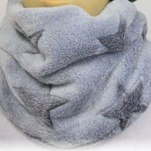Puede incluir: Un cuello de forro polar gris claro con detalles de estrellas bordadas. La bufanda está hecha de un material suave y afelpado, que proporciona calidez y comodidad. El diseño de estrellas añade un elemento decorativo a este accesorio de invierno.