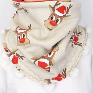 May include: A cream-coloured Christmas scarf with a repeating pattern of cartoon reindeer wearing Santa hats. The scarf is trimmed with white pom-poms and has a red lining. The reindeer have brown antlers, red noses, and smiling faces.