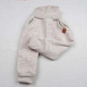 Op de afbeelding: Beige broek met een textuur, een hoge geribbelde tailleband, geribbelde enkelboorden en gladde stoffen accenten bij de zakken. Een klein bruin rechthoekig label is bevestigd aan de rechterzak. De tekst niciart design is linksboven zichtbaar.