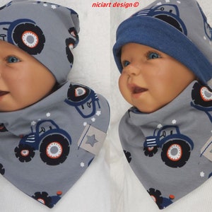 Può includere: Un set di cappello e bavaglino per neonato grigio e blu con stampa di trattore. Il cappello ha un bordo blu pieghevole e il bavaglino ha una stella nell'angolo.