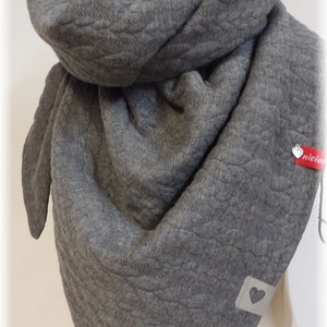 Könnte beinhalten: Grauer Strick Schal mit einem strukturierten Muster. Der Schal ist gefaltet und auf einer Holzpuppe ausgestellt. Der Schal hat ein kleines herzförmiges Etikett.
