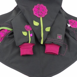 May include: A dark grey jacket featuring magenta flower appliqués with green stems and leaves. The jacket has magenta ribbed cuffs, a hood with a large floral design, and a pocket with a magenta patterned interior and a bright green trim.