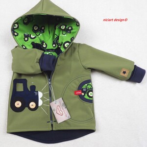 Può includere: Una giacca verde con cappuccio, cerniera blu e un design di trattore sul davanti. Il cappuccio è foderato con un tessuto verde con stampa di trattore. La giacca ha una stella sulla manica destra e il testo "niciart design ©" sul lato destro dell'immagine.