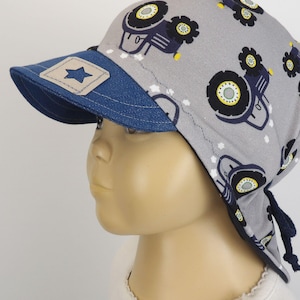Op de afbeelding: Een grijze en blauwe baseballpet met een blauwe denimklep en een ster aan de voorkant. De pet heeft een grijze stoffen strik aan de achterkant en een patroon van blauwe tractoren op de grijze stof.