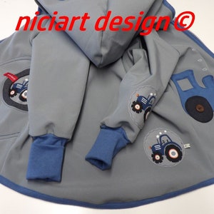 Può includere: Una giacca grigia con cappuccio e bordi blu e applicazioni di trattori blu. La giacca ha una cerniera e un cappuccio. Il testo "nicart design@" è visibile sulla giacca.