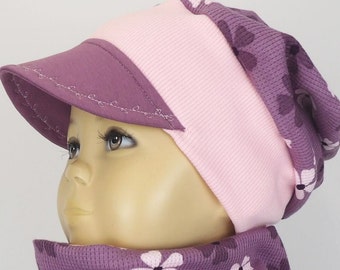 May include: A pink and purple knitted hat with a visor. The hat has a floral pattern on the back and a stitched seam around the visor.