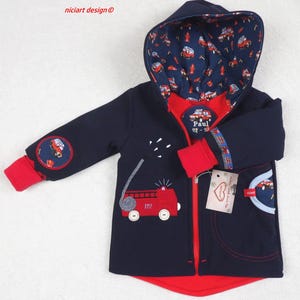 Op de afbeelding: Marineblauwe jas met capuchon en rode voering en accenten. De jas heeft een rode brandweerwagen applicatie met het nummer 112, een brandslang en een patch op de mouw. De capuchonvoering en de zak hebben een brandweerwagenpatroon.