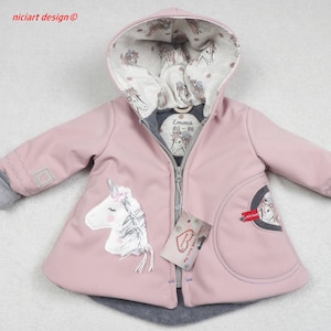 Könnte beinhalten: Rosa Kapuzenjacke mit Einhorn-Applikation. Die Jacke hat einen grauen Reißverschluss, Bündchen und ein Kapuzenfutter mit Pferdemuster. Das Etikett lautet "Emma 80-86".
