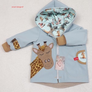 Può includere: Una giacca per neonati blu chiaro con un'applicazione di giraffa marrone sul davanti. La giacca ha un cappuccio e una cerniera. L'interno del cappuccio è foderato con un tessuto blu chiaro e bianco con stampa di giraffa. La giacca ha una tasca marrone sul lato sinistro con un'etichetta rossa che dice "nicicart".