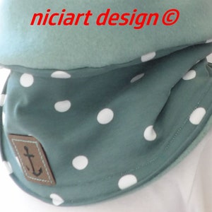 Könnte beinhalten: Ein türkisfarbener Halsschmeichler mit weißen Punkten und einem braunen Lederflicken mit einem Anker-Symbol. Der Text "niciart design @" ist oben auf dem Halsschmeichler sichtbar.