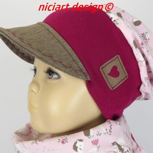 Könnte beinhalten: Eine rosa und braune Mütze mit einem braunen Visier und einem kleinen braunen Herz-Patch. Die Mütze hat ein rosa Blumenmuster auf der Innenseite.