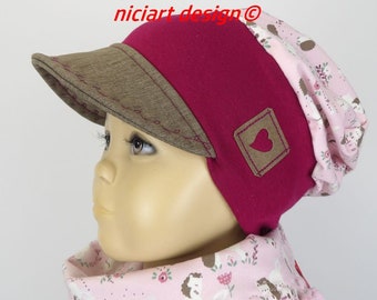 May include: A pink and brown beanie with a brown visor and a small brown heart patch. The beanie has a pink floral pattern on the inside.