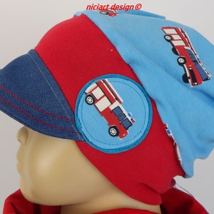 Può includere: Un cappello rosso e blu a tema pompiere con una tesa in denim. Il cappello presenta una toppa circolare con un'illustrazione di un'autopompa. La corona del cappello è azzurra con un motivo di autopompa.