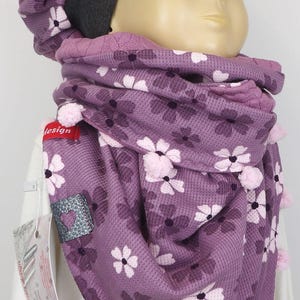 Puede incluir: Una bufanda de punto morada con un patr&oacute;n floral y pompones rosas. La bufanda la lleva un ni&ntilde;o que lleva un gorro morado y gris con ala.