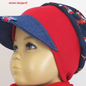 May include: A red and blue beanie with a denim visor and a print of airplanes. The beanie is worn by a child.