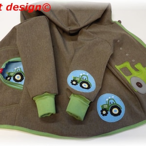 Può includere: Una giacca con cappuccio marrone con rifiniture verdi e una cerniera. La giacca ha diversi patch con trattori verdi. Il testo "niciart design©" è visibile sulla giacca.