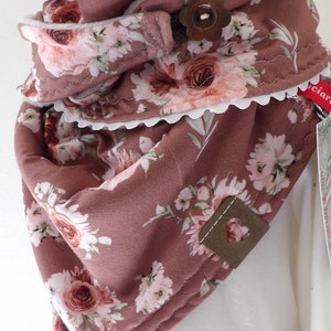 Puede incluir: Una bufanda infinita de color malva con estampado floral de rosas rosas y hojas verdes. La bufanda tiene un ribete de encaje blanco y una etiqueta de cuero marrón con un corazón recortado. El texto "niciart design@" es visible en la bufanda.