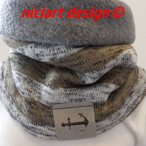 Op de afbeelding: Een gebreide nekwarmer met bruin-witte strepen, een grijze fleecevoering en een leren ankerpatch.