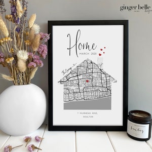 May include: A black framed print with a house-shaped map design. The print includes the word "Home" and the date "MARCH 2020". A vase of dried flowers and a candle are also visible in the image.